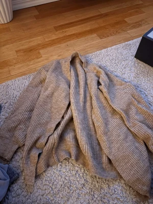 Två ribbstickade koftor i beige & grå - Säljer två mysiga ribbstickade koftor, en i beige och en i grå. Båda har öppen front, lång ärm och avslappnad passform. Perfekta att slänga på sig när det är kyligt ute.