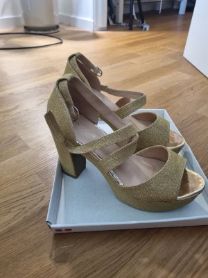 Guldiga högklackade skor  - Snygga guldiga pumps från Dana med glitterfinish och bred klack. Endast använda en gång på min bal. Mycket bekväma och fina! Dma om du har några frågor❤️
