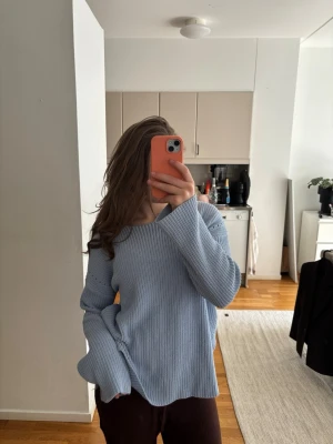 Ljusblå stickad tröja med knyt - Mysig ljusblå stickad tröja med rund hals och långa ärmar. Tröjan har en snygg detalj med knyt i ryggen och en öppning som ger en cool look. Perfekt för att slänga på sig när det är lite kyligt ute.