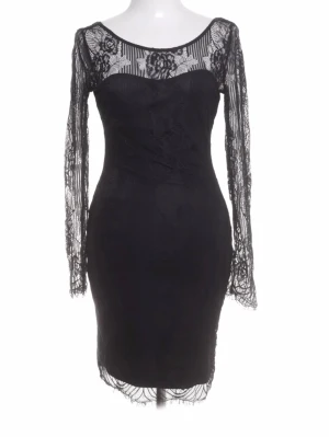 Svart spetsklänning med lång ärm - Elegant svart kortklänning med långärmade spetsdetaljer och transparent överdel. Klänningen har figurnära passform, rundad halsringning och vackra blommiga spetsmönster på ärmar och axelparti. Perfekt för dig som vill ha en stilren och sofistikerad look.