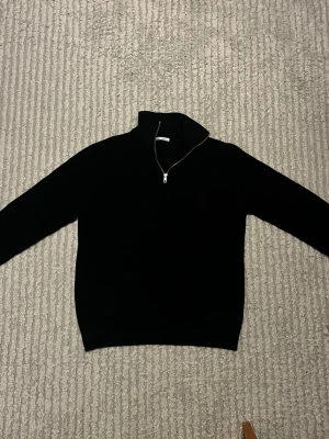 Marinblå stickad halvzip-tröja - Säljer en mörkblå stickad tröja med halvzip och hög krage från Zara, tröjan har långa ärmar och ribbade muddar vid ärmslut och nederkant. Tröjan är knappt använd. Hör av dig vid funderingar!