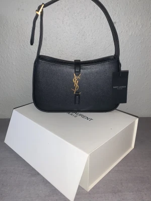Svart YSL axelremsväska i läder - Tjena där! Jag säljer denna Saint Laurent YSL väskan då jag köpte den åt min mamma men hon tyckte den var för liten då hon är lite mer åt den äldre/omoderna sidan. Så om du är intresserad av denna väska så är det bara att höra av dig! Pris kan såklart diskuteras vid snabb försäljning, ha det gott!🙌🙌