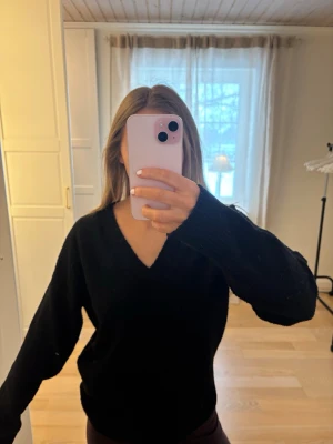 Svart stickad V-ringad tröja - Säljer en svart stickad tröja med V-ringning och långa ärmar. Tröjan har en avslappnad passform och kan bäras både på axeln eller off-shoulder. 