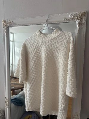 Grädd-vit strukturerad tröja med halvpolokrage - Säljer en grädd-vit tröja med unik strukturerad yta och halvpolokrage. Tröjan har halvlånga ärmar och är tillverkad i ett mjukt, texturerat material som ger en cool och modern look. Perfekt för dig som gillar stilrena plagg med det lilla extra. Helt ny (ord. pris 409kr)