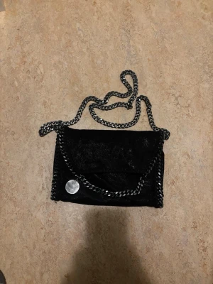 Svart axelväska med kedja - Snygg svart axelväska med silverfärgad kedja och dekorativ kant. Väskan har ett lock med magnetknäppning och ett innerfoder med leopardmönster samt innerficka med dragkedja. Perfekt för dig som gillar trendiga detaljer och cool stil.