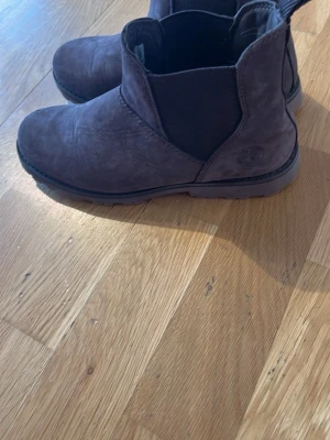 Bruna Chelsea boots Timberland mocka - Snygga bruna Chelsea boots från Timberland i mocka med elastiska paneler på sidorna och robust sula. Klassisk rund tå och diskret Timberland-logga på hälen. Perfekta för dig som vill ha en stilren och bekväm sko till vardagslooken.