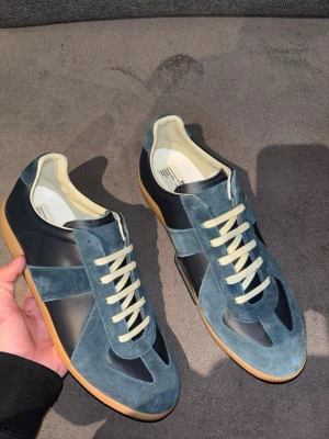 Maison Margiela gats  - Stilrena mörkblå sneakers från Maison Margiela med ovandel i mocka och skinn, beige innersula och vita snören. Klassisk siluett med gummisula och diskreta detaljer som ger en exklusiv känsla. Perfekta för dig som gillar minimalistisk design. Allt og ingår samt orderbevis bilder från goat.  Storlek 44, Ställ frågor!!