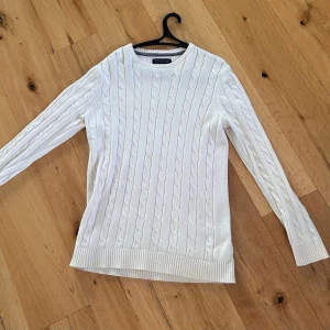 Vit kabelstickad tröja Jack & Jones - Vit kabelstickad tröja från Jack & Jones. Tröjan har rund halsringning, långa ärmar och ribbade muddar vid ärmslut och nederkant. Perfekt för dig som gillar stilren design i mjukt material. Passar L/M.