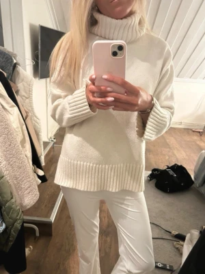 Vit polotröja med grovstickad krage - Säljer en stilren vit stickad polotröja med bred ribbad krage, muddar och nederkant. Tröjan har en avslappnad passform och är gjord i mjukt material, perfekt för kalla dagar. Enkel att matcha och supermysig att bära.