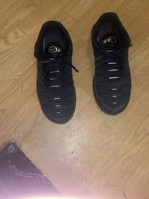 Svarta Nike Air Max tns - Säljer ett par svarta Nike Air Max Plus sneakers med mesh- och syntetmaterial, klassisk TN-logga på plösen och vågformade detaljer på sidorna. Skorna har en chunky sula och lågt skaft för en sportig look.