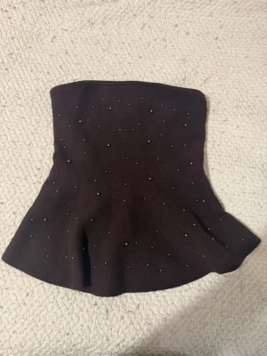 Brun stickad tubtopp med pärlor - Säljer en brun stickad tubtopp dekorerad med små pärlor över hela plagget. Toppen har en lätt utsvängd form nedtill och är perfekt för att skapa en trendig look. Superfin att styla med både jeans och kjol!