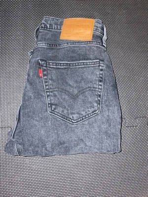 Levis 502 - Säljer ett par svarta skinny jeans från Levi's med klassisk femficksdesign och läderpatch bak i midjan. Jeansen har en tvättad look och smal passform som sitter snyggt längs benen. Perfekta till en avslappnad streetstyle. W29 L32 använda en gång
