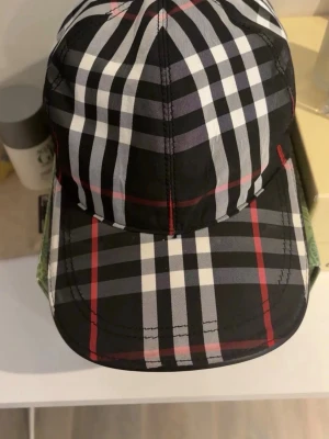 Rutig keps med svart, vitt och rött - Snygg keps med klassiskt rutigt mönster i svart, vitt och rött. Justerbar rem baktill för perfekt passform. Tillverkad i ett lätt och bekvämt material, perfekt för att lyfta din streetwear-look.