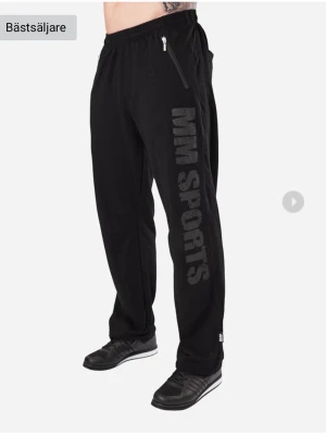 MM Sports byxor - Säljer ett par svarta mjukisbyxor från MM Sports med stort tryck längs benet och dragkedjeförsedda fickor framtill. Byxorna har resår i midjan och bakfickor. Perfekta för gymmet eller chill hemma. Materialet är mjukt och bekvämt, troligen bomullsmix. Storlek: L Skick: Helt nya. Nypris: 600kr