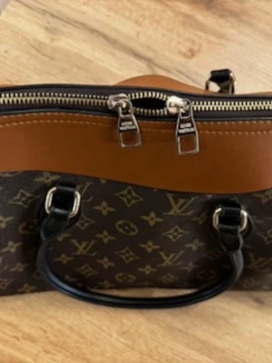 Louis Vuitton Monogram handväska - Snygg handväska från Louis Vuitton i klassiskt brunt monogrammönster med detaljer i cognacsfärgat och svart läder. Väskan har dubbla handtag och silverfärgade metalldetaljer samt dragkedja upptill. Perfekt för dig som gillar lyxiga accessoarer.