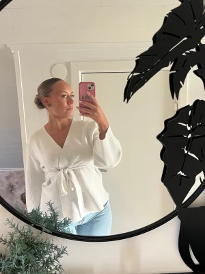 Vit omlottblus med knytband - Snygg vit stickad kofta med knytband i midjan och v-ringning. Koftan har långa ärmar och är tillverkad i ett mjukt, tjockare material.