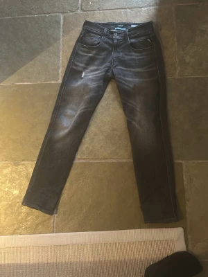 Replay svarta slim fit jeans - Säljer ett mörk grå svarta slim fit jeans från Replay med snygga slitningar och tvättade detaljer. Jeansen har klassisk femficksmodell och raka ben. Materialet är mjukt och stretchigt för extra komfort. Perfekta för en trendig och avslappnad look.