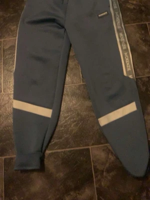 Blå tracksuit från McKenzie: Storlek S - Snygg tracksuit från McKenzie med vita detaljer.  Perfekta för chill eller träning.  Man får Byxor, T-Shirt och Hoodie för väldigt generöst pris! 