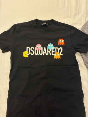 Svart DSQUARED2 Pac-Man t-shirt - Svart t-shirt från DSQUARED2 med färgglada Pac-Man-figurer och stort vitt tryck på bröstet. Klassisk rund hals och korta ärmar. Tillverkad i mjuk bomull som känns skön mot huden. Perfekt för dig som gillar retro och streetstyle.