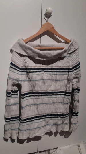 Off-shoulder tröja - En stickad, randig off-shoulder tröja. Har två hål, en på övre baksidan och en i ena armhålan.