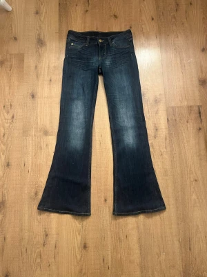 Mörkblå bootcut jeans från Weekday - Säljer ett par mörkblå bootcut jeans från Dr. Denim med klassisk femficksmodell och lätt slitna detaljer framtill. Jeansen har utsvängda ben och guldfärgade knappar. Perfekta för dig som gillar retrovibbar och en avslappnad look.