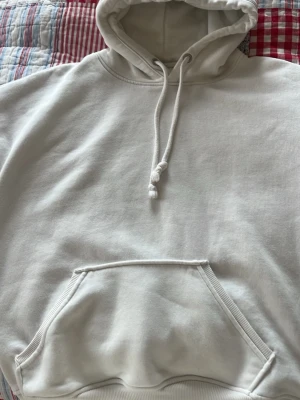 Vit hoodie med magficka och huva - Snygg vit hoodie med klassisk magficka . Tillverkad i mjukt bomullstyg med ribbade muddar vid ärmsluten. Perfekt för en avslappnad och basic stilen. Inga fläckar eller missfärgningar