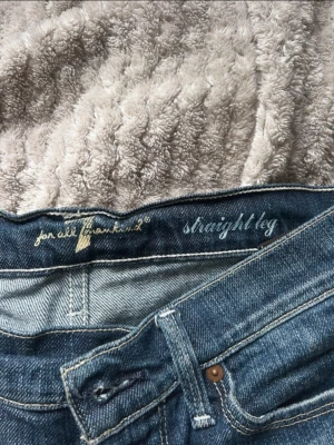 Blå straight leg jeans från 7 For All Mankind - Säljer ett par klassiska blå straight leg jeans från 7 For All Mankind. Jeansen har snygga röda och gula detaljer på bakfickan och är tillverkade i mjuk bomull. Perfekta för dig som gillar tidlös stil och raka ben.
