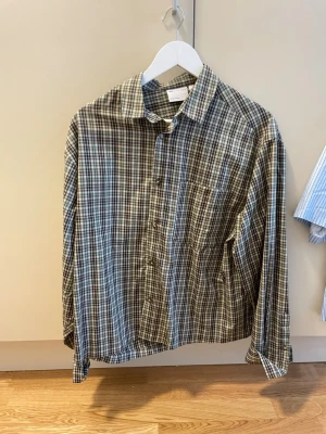 Rutig skjorta i bomull - Snygg rutig skjorta i bomull. Skjortan har klassisk krage, knäppning framtill och en bröstficka. Färgskalan går i brunt, beige och vitt. Perfekt för en avslappnad och trendig look.