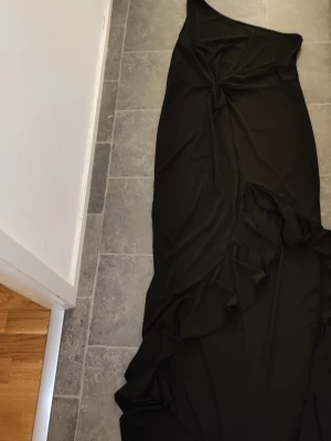 Svart långklänning med twistdetalj - Säljer en svart långklänning med twistad detalj framtill. Klänningen har ärmlös design och en elegant, enkel siluett som faller snyggt längs kroppen. Perfekt för dig som gillar stilrena plagg med en liten twist.