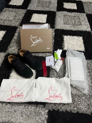 Svarta sneakers från Christian Louboutin - Stilrena svarta sneakers från Christian Louboutin i mocka med klassisk låg siluett. Skorna har svarta skosnören, diskret sömnad och beige innersula. Kommer med originalkartong, dustbags och tillbehör. Perfekta för dig som gillar exklusiva och tidlösa sneakers.