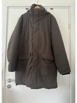 Brun jacka / kappa med utfällbar huva, Dressman - Varm och skön brun vinterjacka / kappa från Dressman i storlek 2XL / XXL. Praktisk utfällbar huva och dubbelgängad dragkedja fram så man kan öppna både uppifrån och nerifrån. Massa bra fickor och interna fack för praktisk förvaring. Mycket gott skick, som ny.   Hämtas i Stockholm eller skickas mot porto.