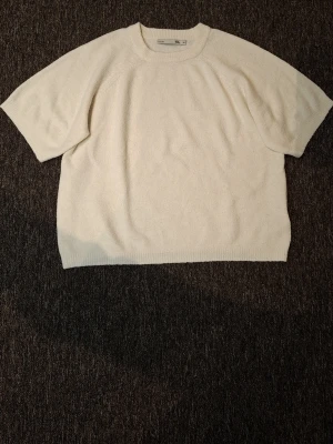 Vit stickad topp från 157 - En enkel och stilren vit stickad topp från 157 med rund halsringning och korta ärmar. Perfekt till jeans eller kjol för en clean look. Mjuk och bekväm med avslappnad passform.