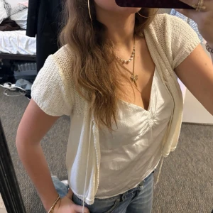 Kortärmad stickad bolero i offwhite - Snygg kortärmad stickad bolero i offwhite med öppen front och luftig struktur. Perfekt att slänga över ett linne eller topp för en chill och trendig look. Materialet känns mjukt och lätt, vilket gör den skön att bära under varmare dagar.