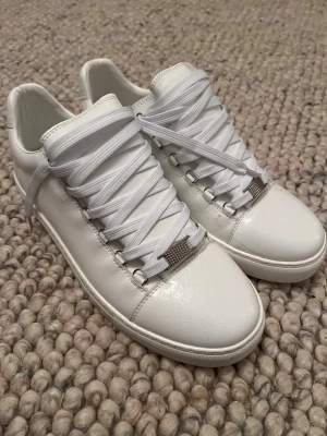 Balenciaga Arena  - Balenciaga Arena – storlek 43 (passar även 44) Stilrena helvita Balenciaga Arena i mycket bra skick. Klassisk och tidlös modell i mjukt läder med hög komfort. Använda varsamt och väl omhändertagna. Passar perfekt för dig som vill ha ett exklusivt par sneakers som funkar till allt. Sälja pågrund av fel storlek 