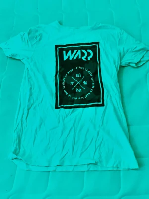 t-shirt med tryck från Warp - Vit t-shirt från Warp med stort svart tryck framtill. Klassisk passform och rund halsringning. Perfekt för dig som gillar streetwear och enkel stil. Tillverkad i mjuk bomull som är skön att ha på sig hela dagen.