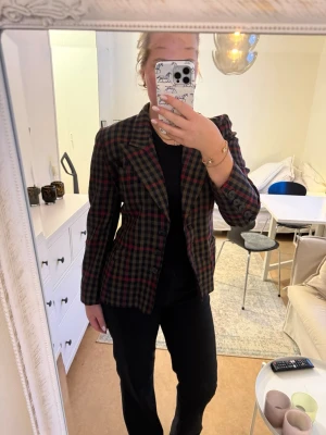 Rutig escada kavaj  - Snygg kavaj i rutigt mönster med inslag av rött, grönt och svart. Klassisk krage och figursydd passform som ger en cool siluett. Perfekt för att lyfta vilken outfit som helst. 