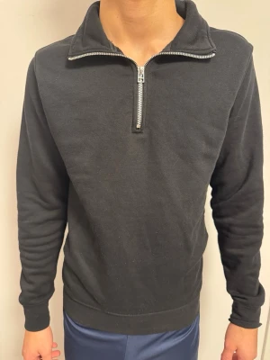 Svart halvzip piké - En stilren svart hoodie med halvzip och hög krage. Tillverkad i mjukt bomullsmaterial och har långa ärmar samt ribbade muddar. Storlek XS 