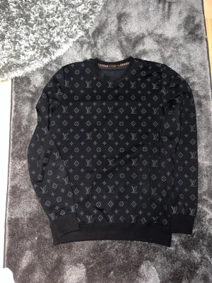 Svart Louis Vuitton sweatshirt - Snygg svart sweatshirt från Louis Vuitton med det klassiska monogrammönstret över hela tröjan. Rund halsringning och ribbade muddar vid ärmslut och nederkant. Perfekt för dig som vill ha en exklusiv och trendig look.Använt 1 gång 
