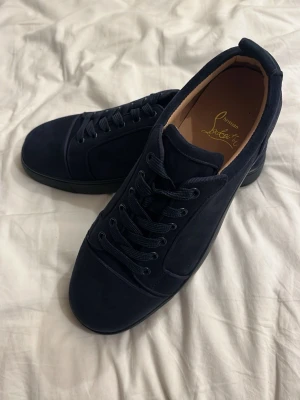 Mörkblå sneakers från Louboutin - Snygga mörkblå sneakers från Christian Louboutin i mocka med klassisk låg siluett. Skorna har matchande diskreta detaljer och den ikoniska röda sulan. Perfekta för dig som vill ha en clean och exklusiv look.