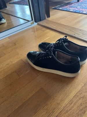 Svarta sneakers med mocka och lack - Snygga svarta lanvin med både mocka och lackdetaljer. Skorna har svarta skosnören, vita sulor och en stilren design som passar till det mesta. Perfekta för dig som gillar en clean och modern look. 