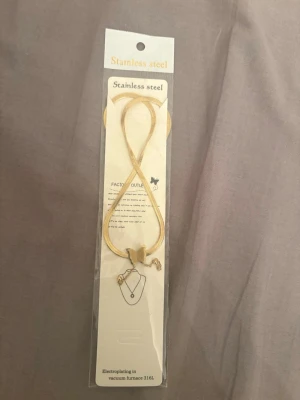 Guldigt halsband i rostfritt stål - Snyggt guldigt halsband i rostfritt stål med en tunn kedja och en liten fjärilsberlock. Halsbandet har justerbar längd och enkel design som passar till många stilar. Materialet är 316L rostfritt stål med elektroplätering.
