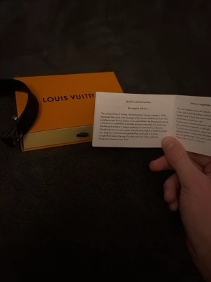 Louis Vuitton monogram armband - Snyggt armband från Louis Vuitton i klassiskt brunt monogrammönster med guldfärgad LV-detalj. Tillverkat i läder och levereras med originalask. Perfekt accessoar för dig som gillar exklusiv och tidlös design.