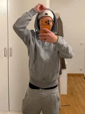 Grå zip-hoodie från Nike - Snygg grå zip-hoodie från Nike med huva och dragsko. Klassisk design med ribbade muddar, fickor framtill och diskret Nike-logga på bröstet. Perfekt för en avslappnad och sportig stil.