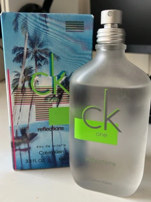 CK One Reflections EdT 100ml - Fräsch och modern parfym från Calvin Klein, CK One Reflections. Flaskan är frostad och har en stilren design med grön logga och detaljer. Kommer i originalkartong med tropiskt motiv. Perfekt för dig som gillar lätta och fräscha dofter.
