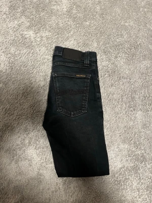 Svarta jeans från Nudie jeans  - Tja, säljer ett par sjukt snygga svarta slim/skinny jeans från Nudie jeans med klassisk femficksdesign och diskret logga på bakfickan. Jeansen har raka ben och är tillverkade i ett mjukt denimtyg som ger en skön passform. Perfekta för dig som gillar en stilren och enkel look. Vid minsta fundering bara att höra av sig! Mvh Rewear collective