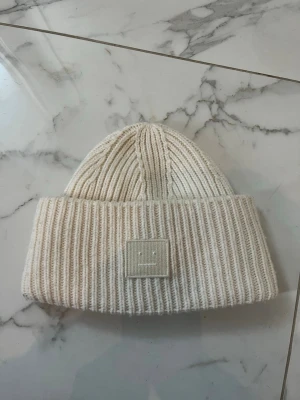 Vit ribbstickad mössa Acne Studios - beige/cremevit acne mössa. den är i jättefint skick förutom lite lite smink inuti. säljer för vill köpa i annan färg. skriv om du har frågor!