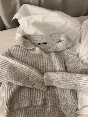 Ljusgrå stickad tröja Gina Tricot - Mysig ljusgrå stickad tröja från Gina Tricot med krage och ribbstickad struktur. Tröjan har långa ärmar och en avslappnad passform, perfekt för lager på lager. Enkel och stilren design som passar till det mesta.