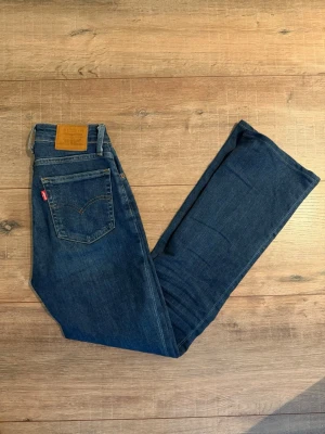 Levi's 725 High Rise Bootcut Jeans - Mörkblå Levi's 725 High Rise Bootcut jeans med klassisk femficksdesign och hög midja. Bootcut-modell som ger en snygg siluett och ikonisk röd Levi's-lapp på bakfickan. Perfekta för dig som gillar tidlös denimstil. Storlek: 24:30