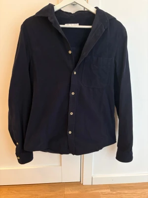 Mörkblå manchesterskjorta - Snygg mörkblå skjorta i mjuk manchester med klassisk krage, bröstficka och knappar framtill. Perfekt för dig som gillar en enkel men stilren look. Långärmad modell som passar till många olika outfits.