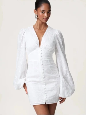 Vit adoore klänning! - Superfin vit kort klänning med v-ringning och långa puffärmar. Klänningen har knappar framtill och ett subtilt blommigt mönster i tyget. Perfekt för sommarens alla tillfällen och ger en romantisk vibe.